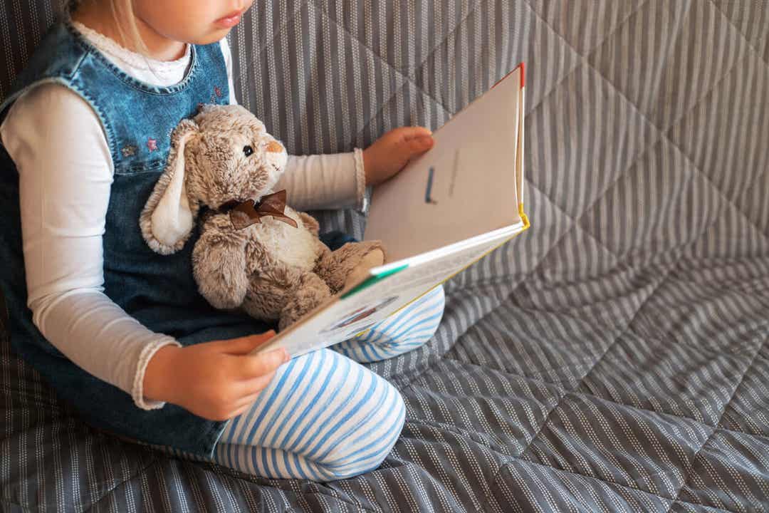 A toddler reading with her stuffed bunny on her lap.