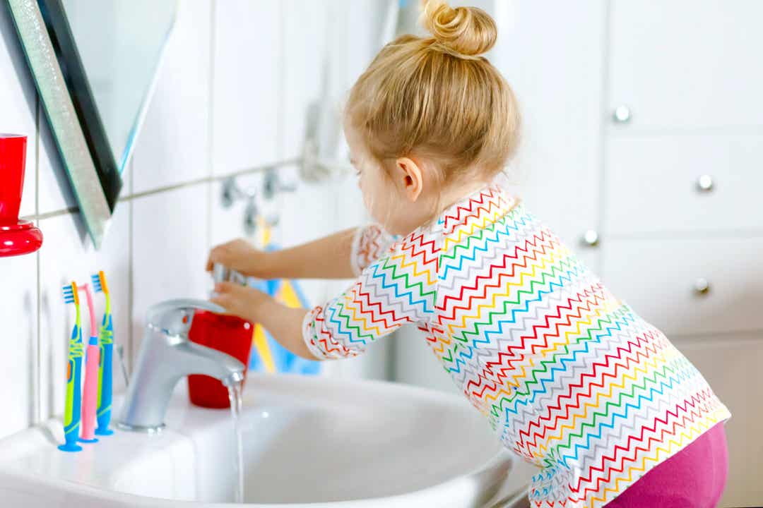 A 3-year-old girl washing her hands in the bathroom sink.