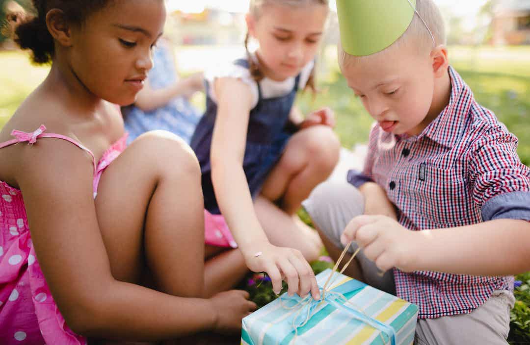 A boy with down syndrome and two other young girls opening a present.