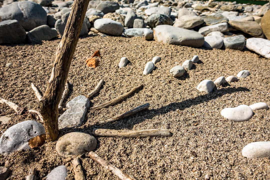 Een zonnewijzer gemaakt van rotsen en stokken op het strand.
