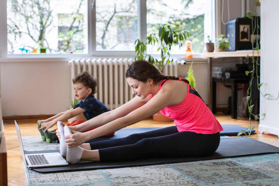 A mother and her young child doing toe touches as they follow an exercise routine on the computer.