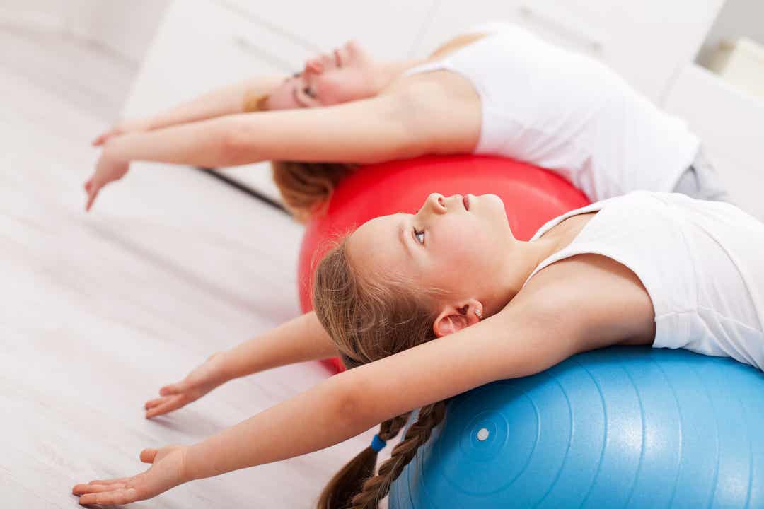 A mother and daughter stretching over exercise balls.
