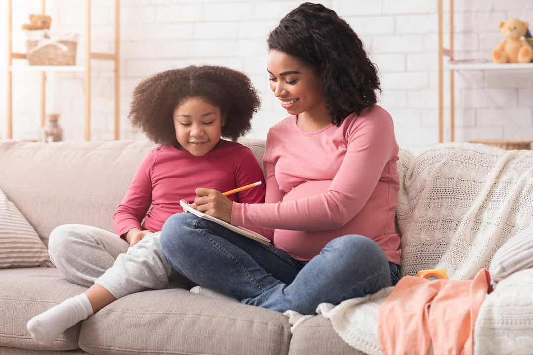 A pregnant woman sitting with her young daughter, choosing names.