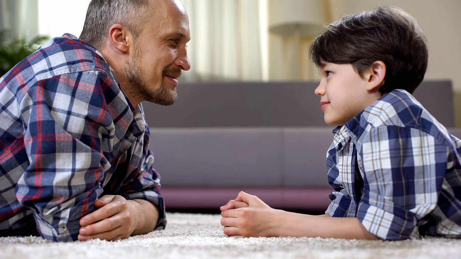 A father and son lying on the floor looking into one another's eyes.
