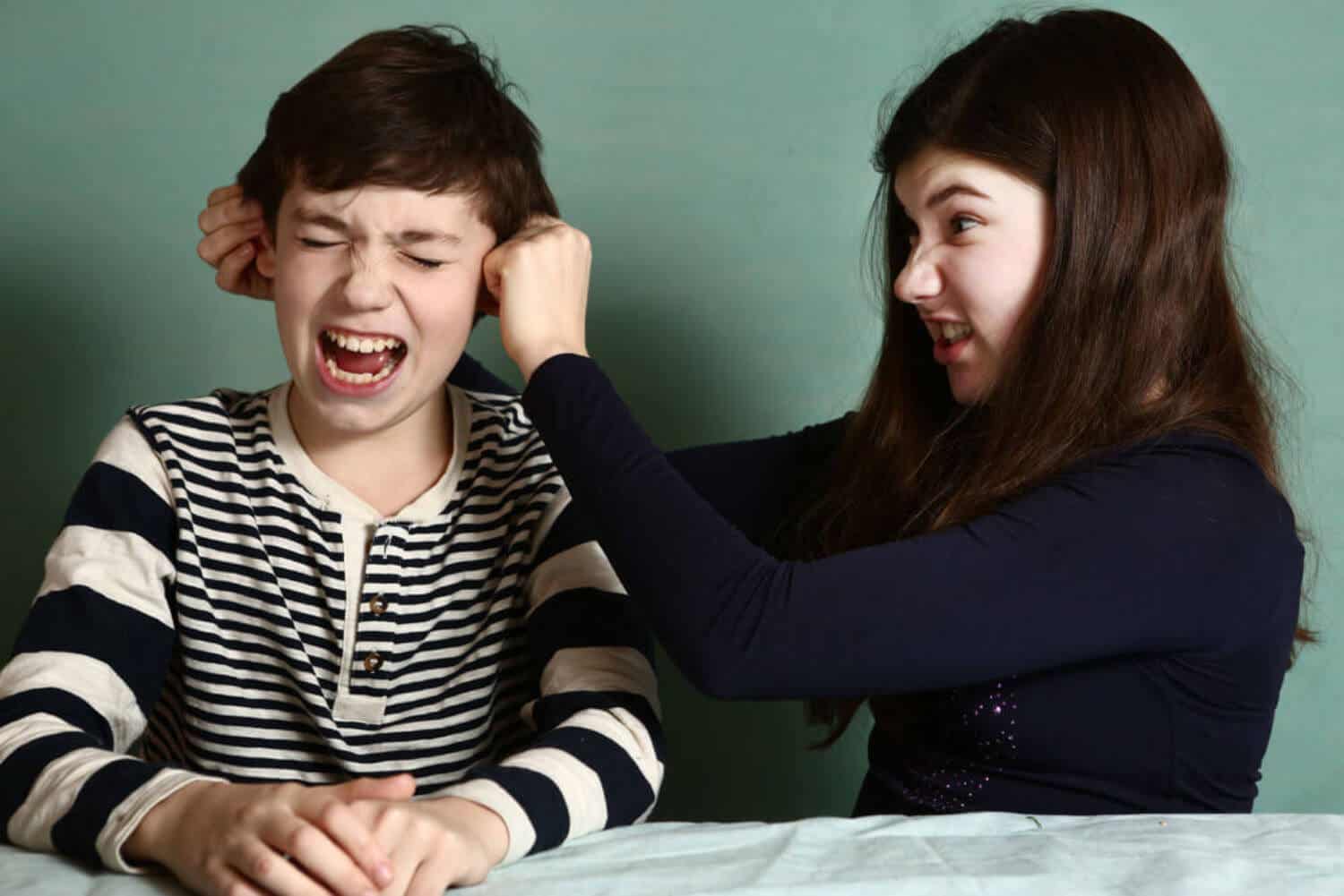 A girl pulling on her brother's ears.