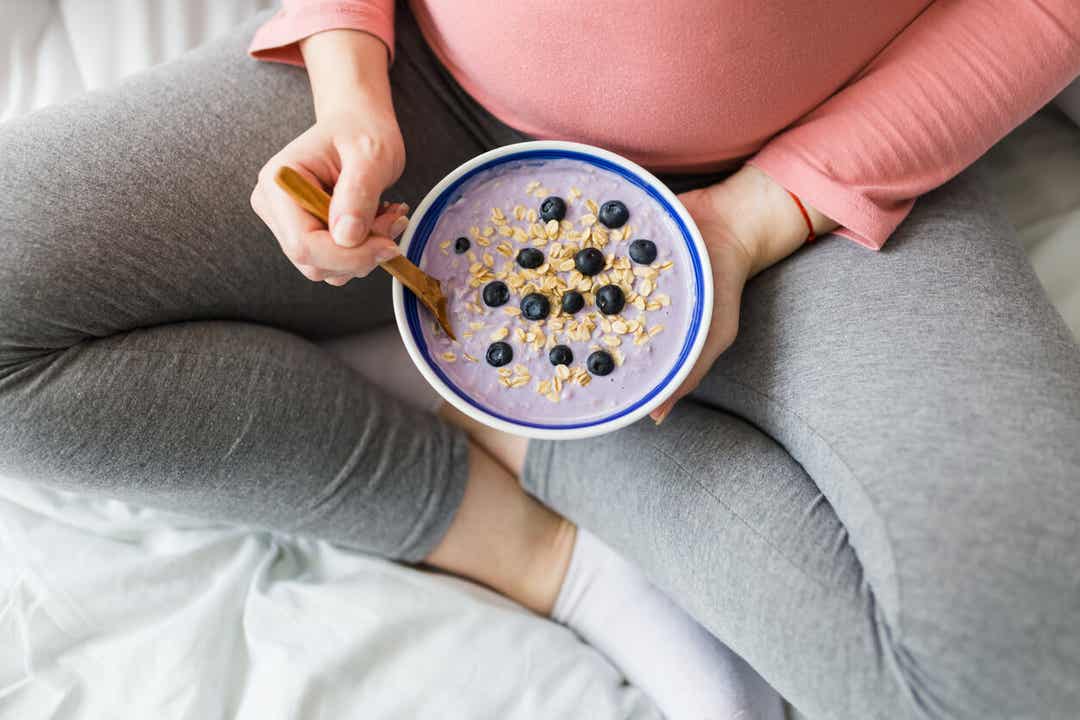 Een zwangere vrouw die granola met yoghurt en fruit eet.