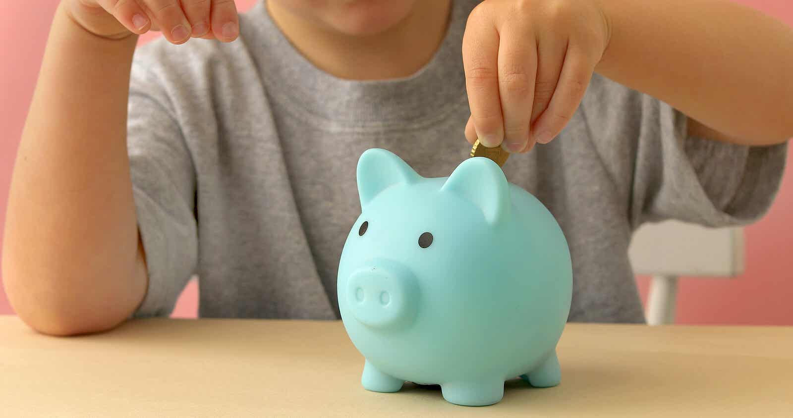 Child putting money into a piggy bank.