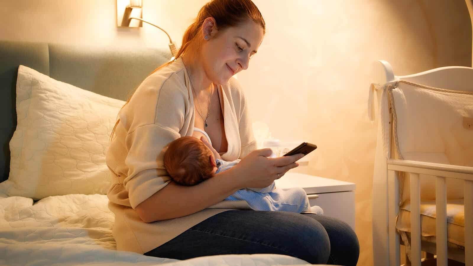 Moeder geeft haar baby borstvoeding terwijl ze enkele apps raadpleegt.