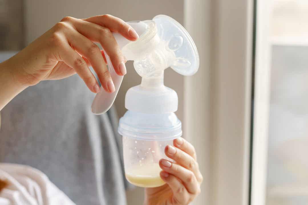 A woman holding a breast pump with milk in the bottle.
