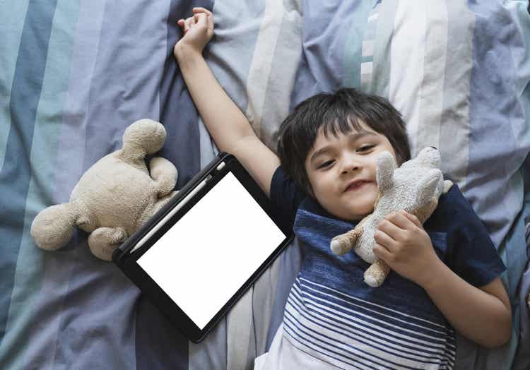 A child laying down next to a tablet.