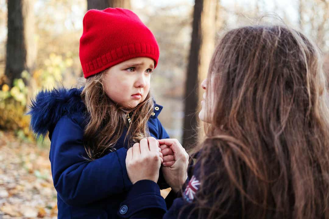 Matka kucająca, by porozmawiać z małą córeczką, która wygląda na zdenerwowaną.