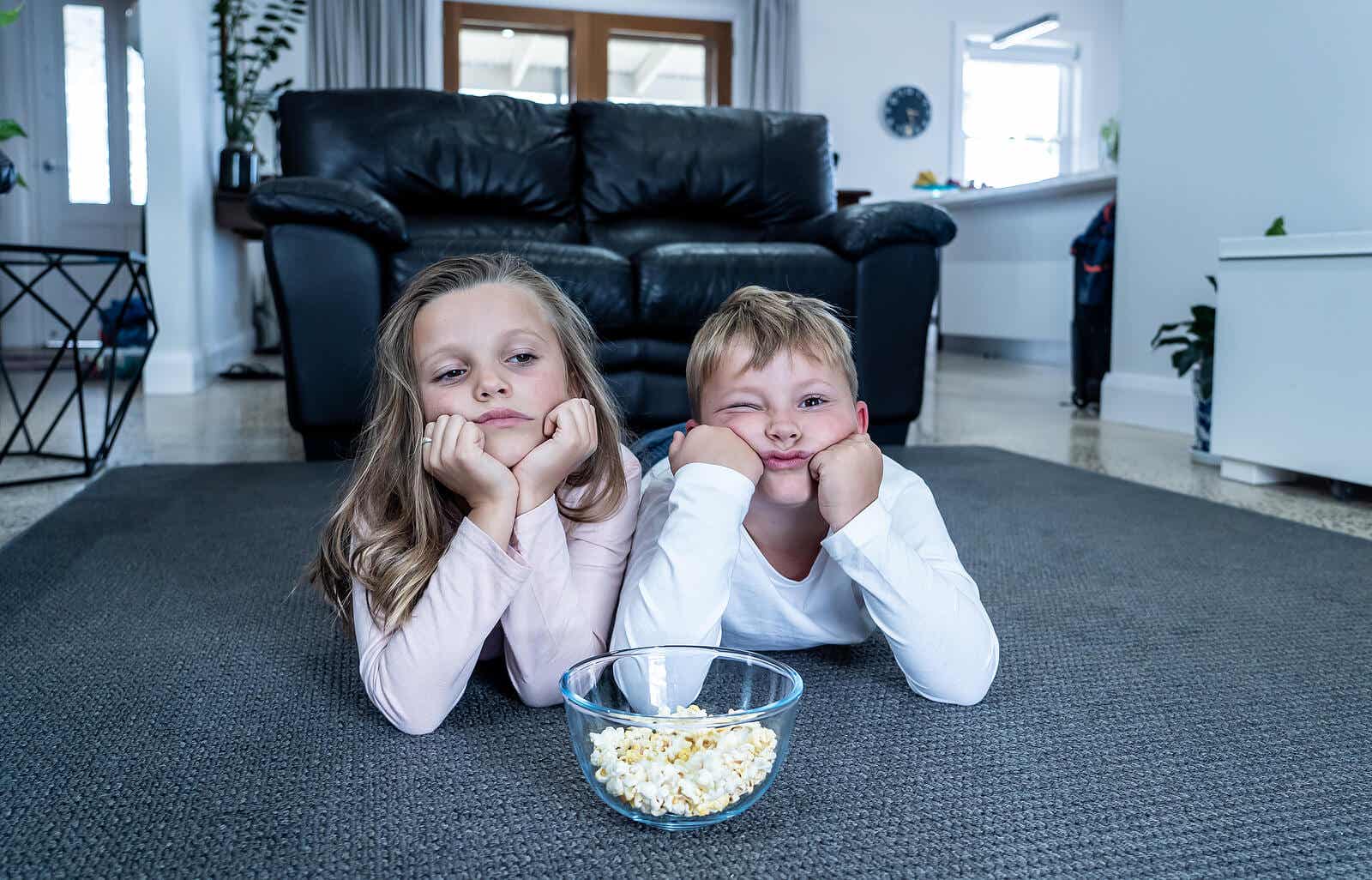 Two bored children eating popcorn in front of the TV.
