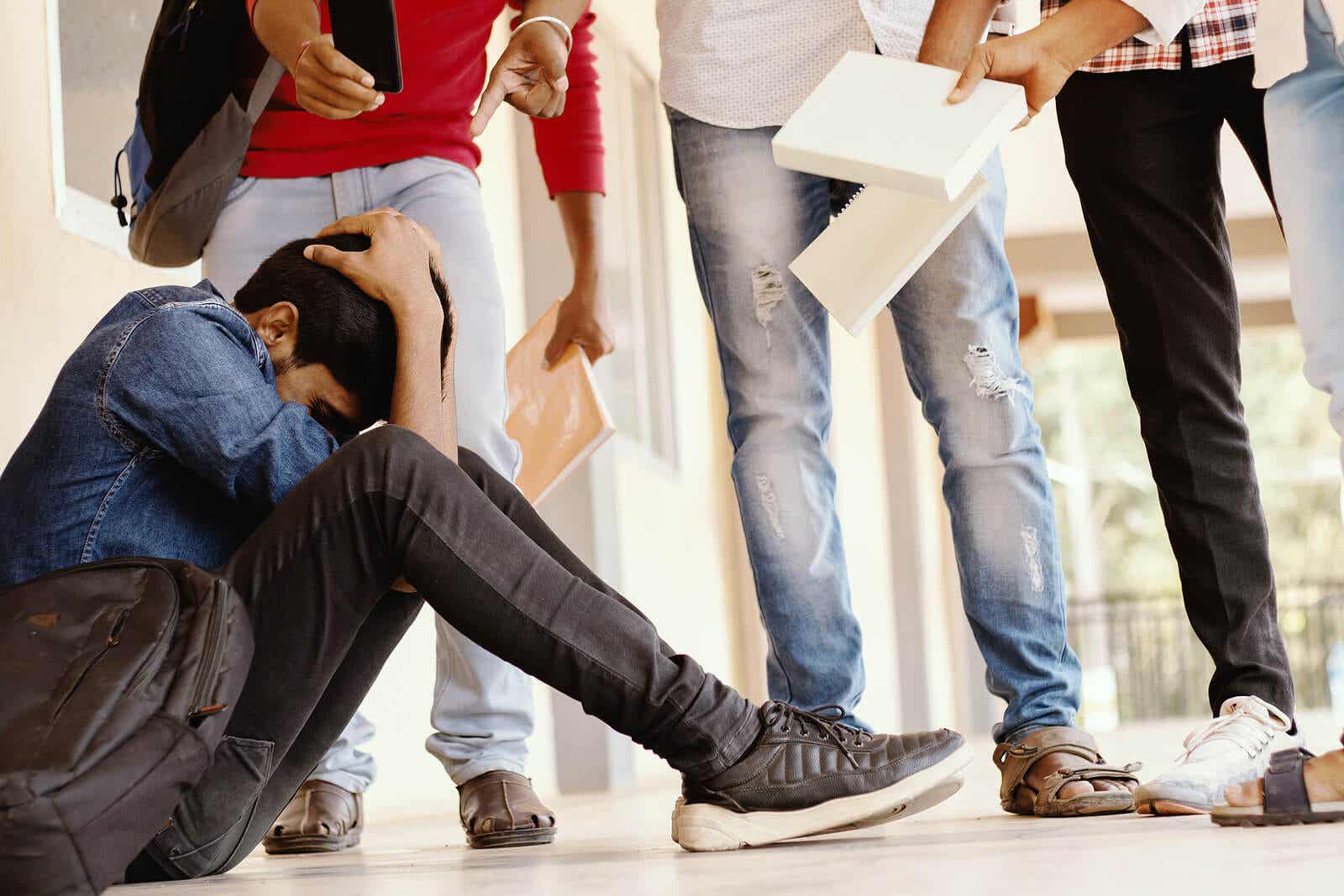 Een tienerjongen die op school op de grond zit, omringd door een groep pestkoppen.