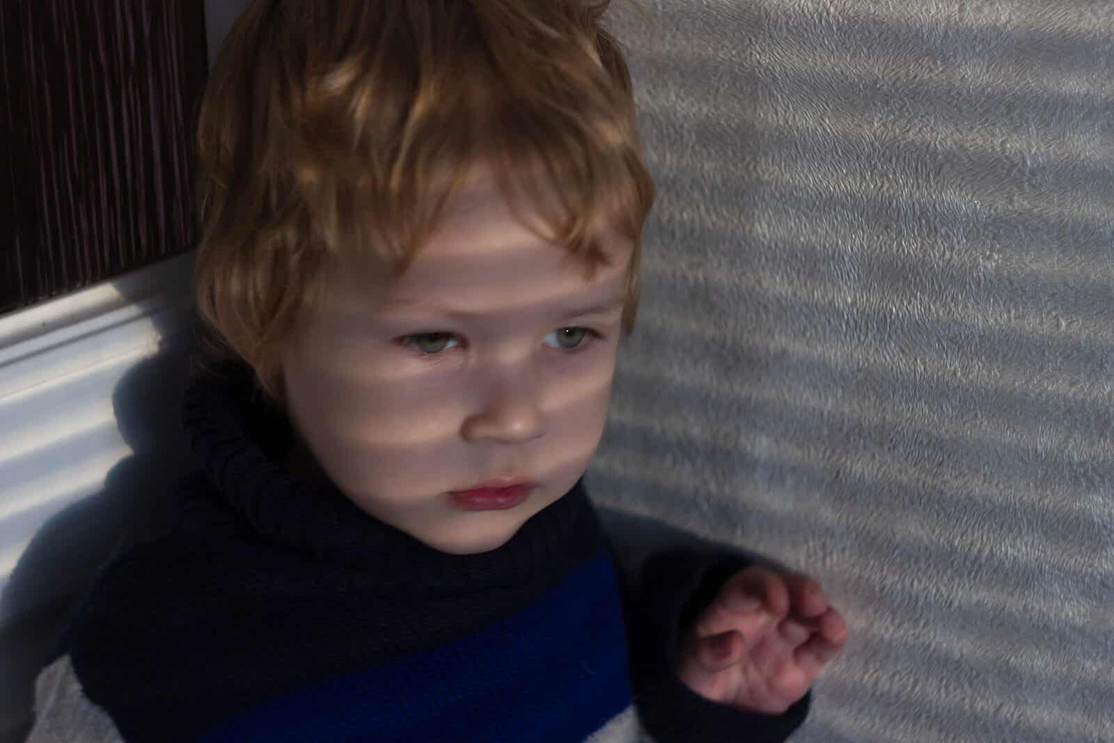 A sensitive toddler boy sitting in a corner.