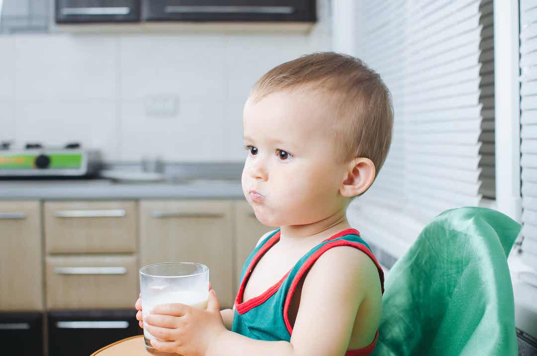Dziecko pijące szklankę mleka w swoim krzesełku.