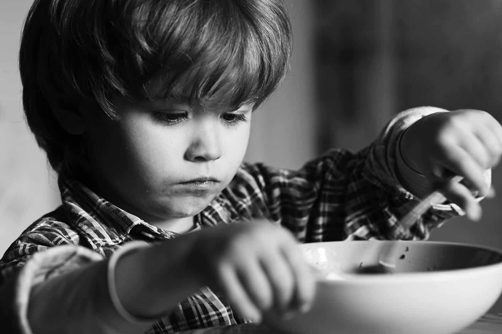 A black and white photo of a child eating a bowl of food with a serious face.