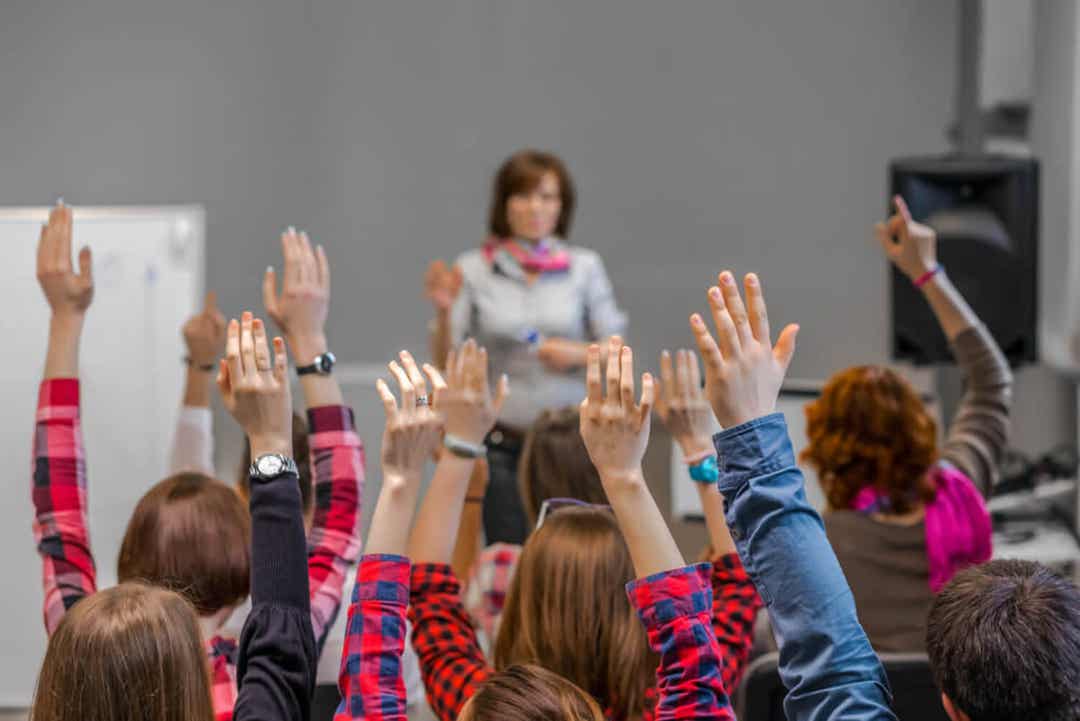 Adolescent students eagerly raising their hands in class.