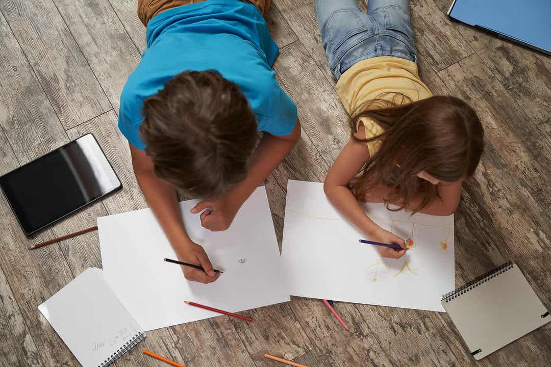A boy and a girl lying on the floor drawing.