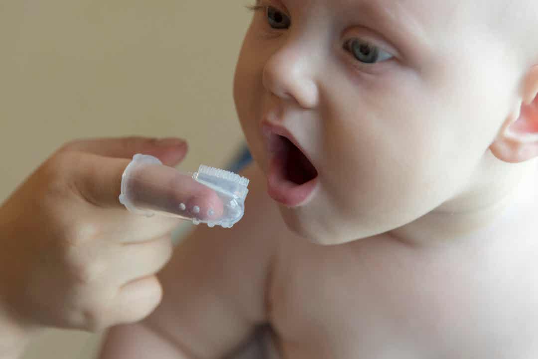 Een moeder die een vingerborstel gebruikt om het tandvlees van haar baby schoon te maken.