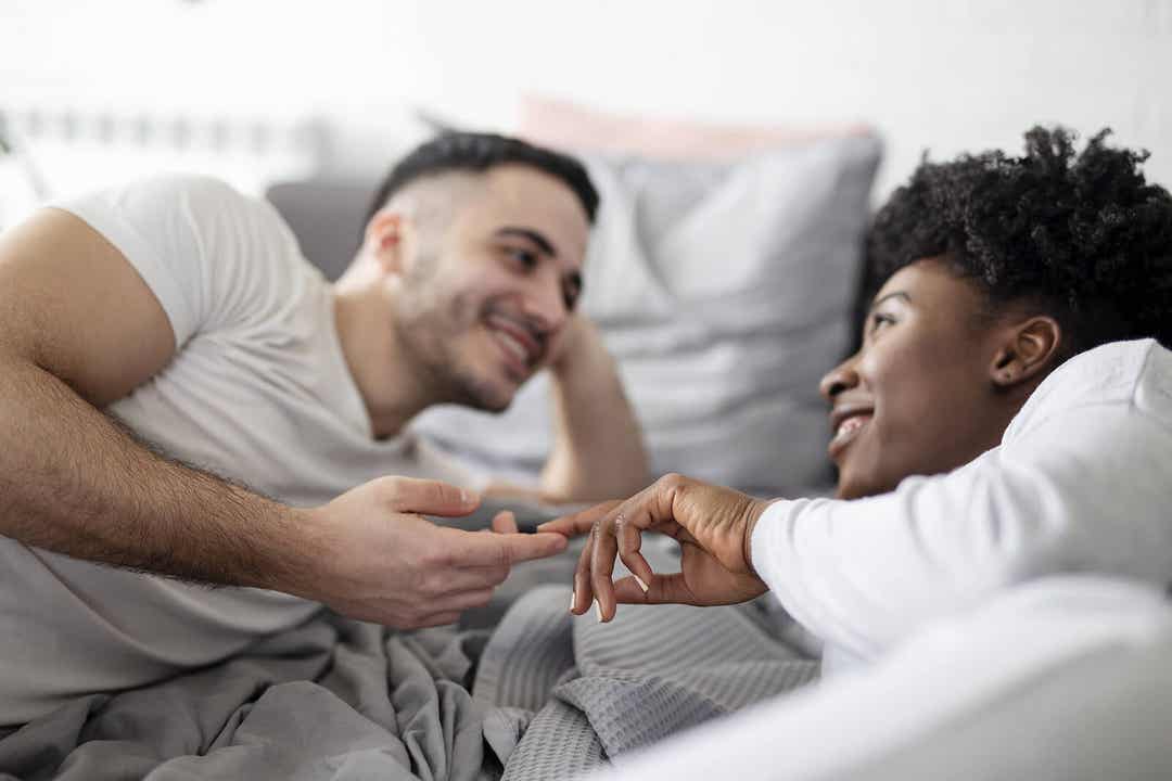 Para dotykająca opuszków palców i patrząca sobie w oczy w łóżku.