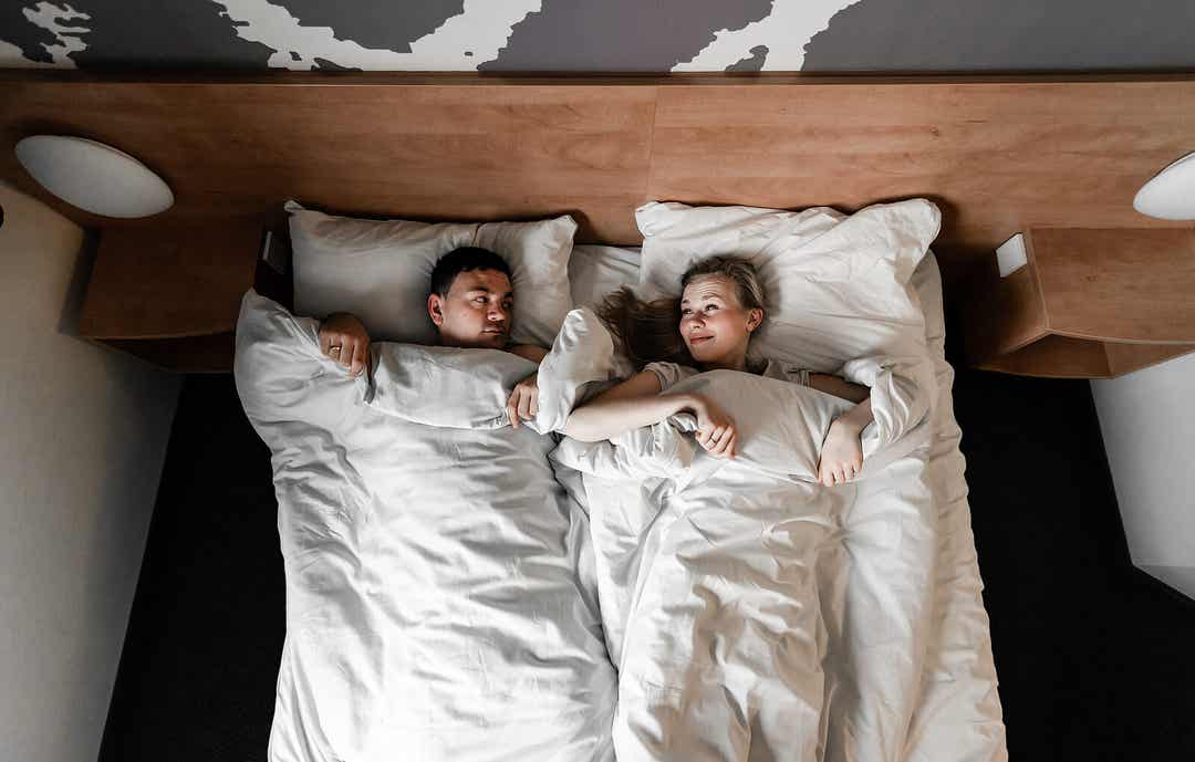 A woman putting a pillow between her and her husband in bed.