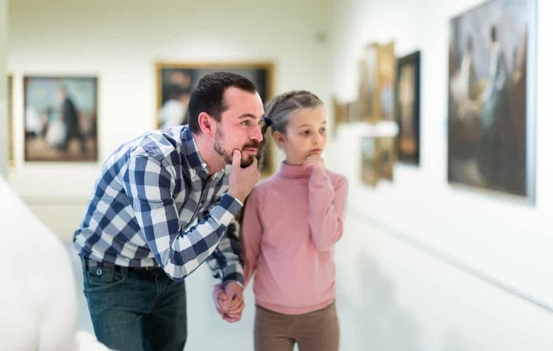 A father and his daughter looking at a painting in a museum gallery. 
