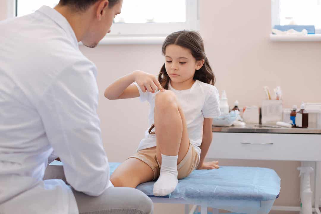 A young girl in the pediatrician's office pointing to her knee.