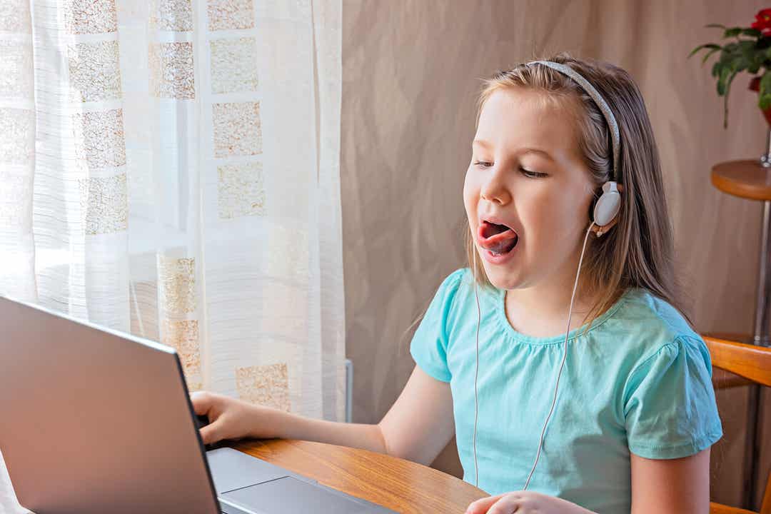 Een jong meisje doet tongoefeningen tijdens een online logopediesessie.