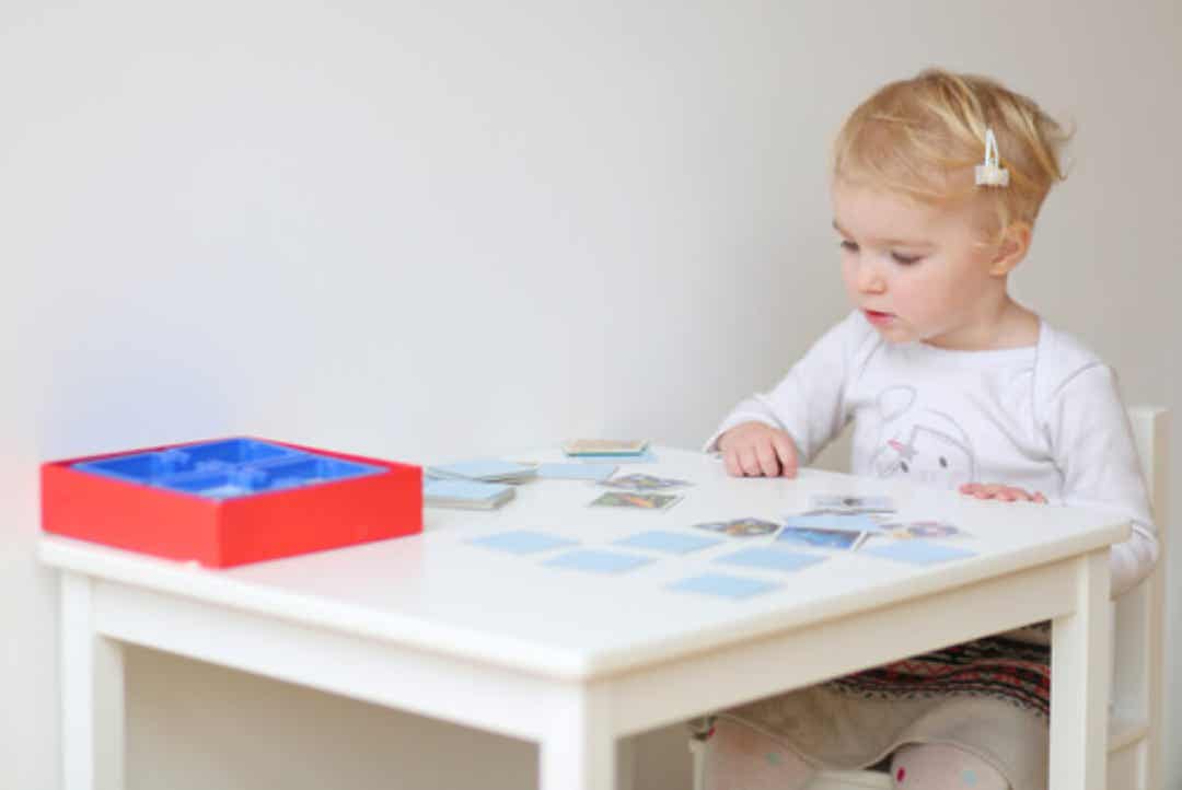 Een peuter die aan een tafel zit te spelen met geheugenkaarten.