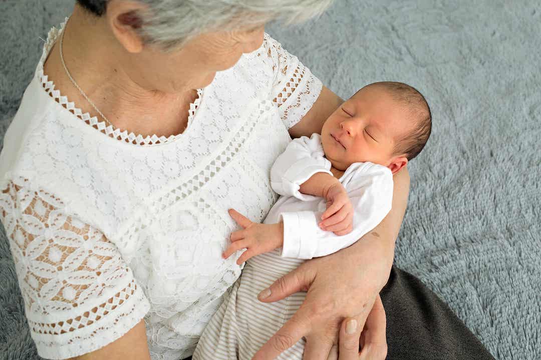 Een grootmoeder die neerkijkt op haar pasgeboren kleinkind in haar armen.