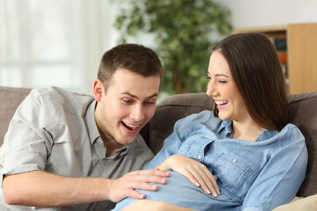 A father smiling with his hand on his partner's pregnant belly.