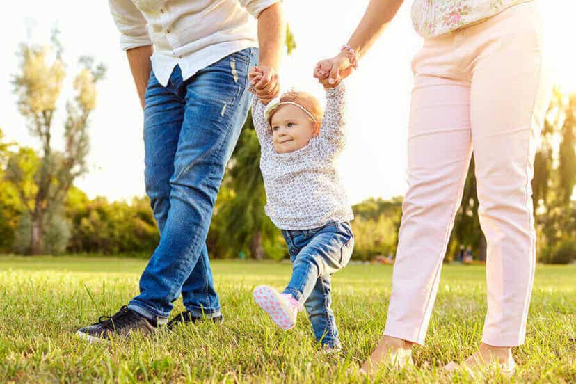 A toddler learning to walk, holding on her mom and dad's hands.
