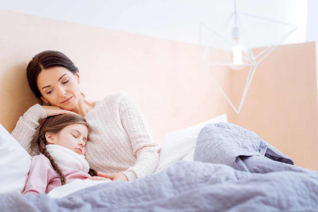 A mother snuggling her young daughter in bed.