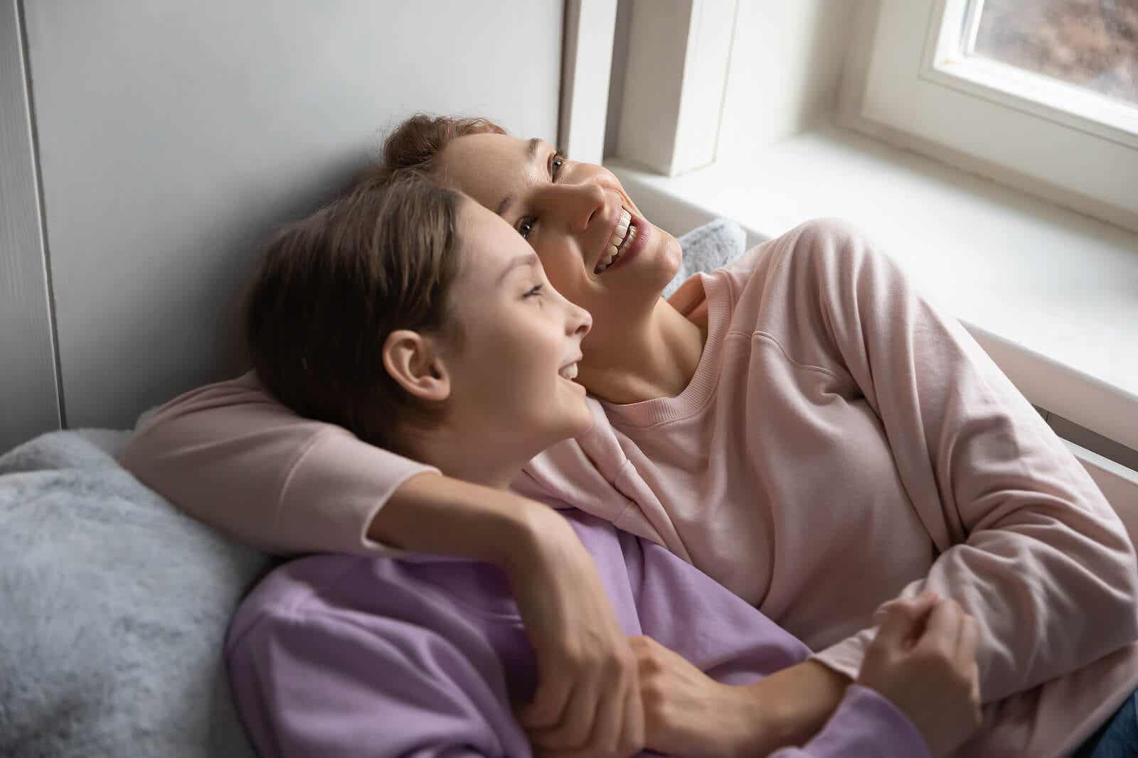 A mother and daughter lying on the couch, smiling out the windown.