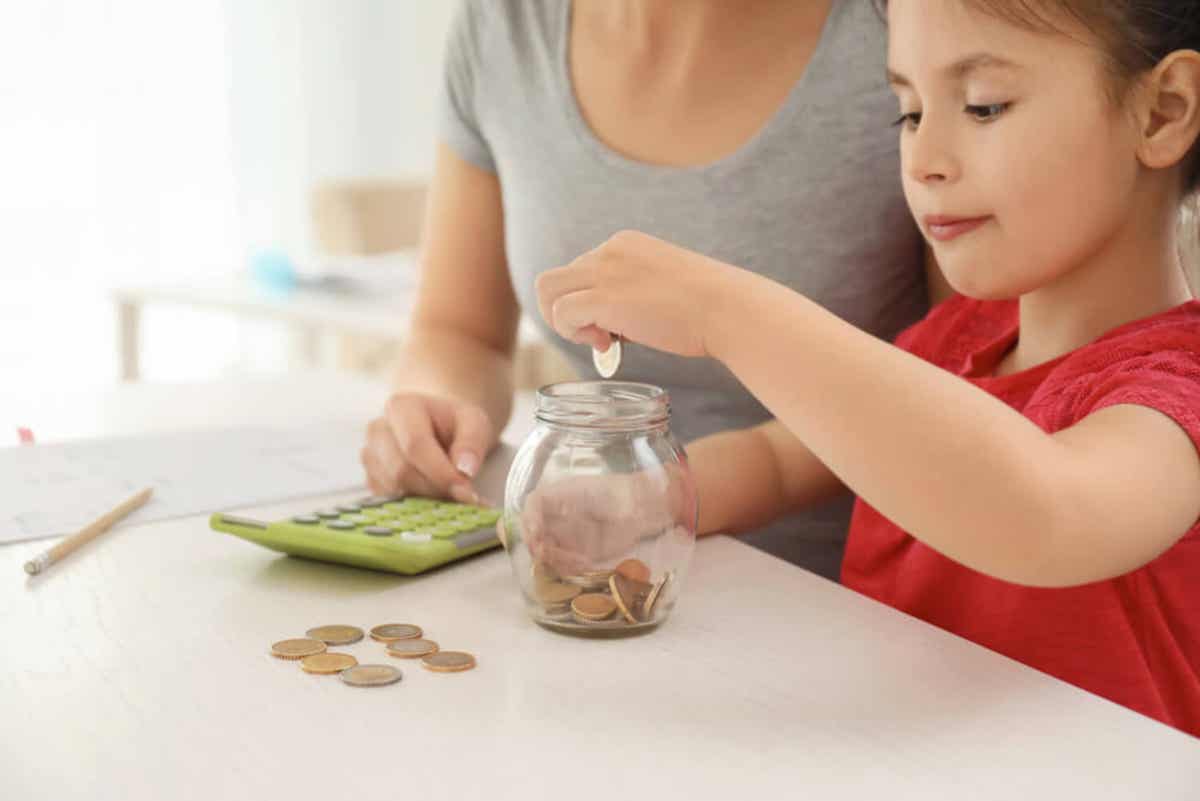 A mother using a calculator while her young daughter drops change into a jar.