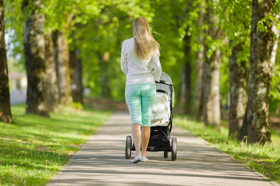 A mother walking down a path in the park with her baby in a stroller.