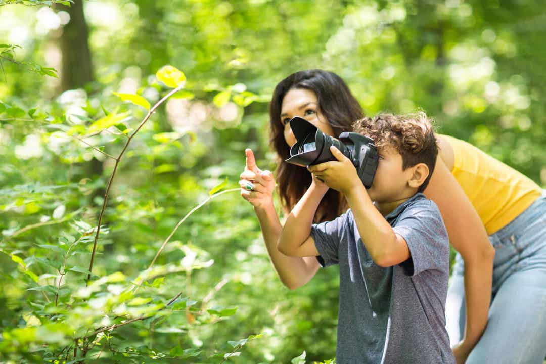 A boy taking pictures in the woods with his mom.