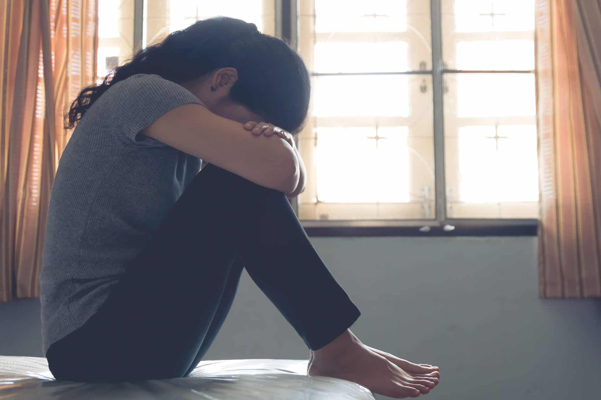 Een vrouw met postpartumdepressie die op haar bed zit te huilen.