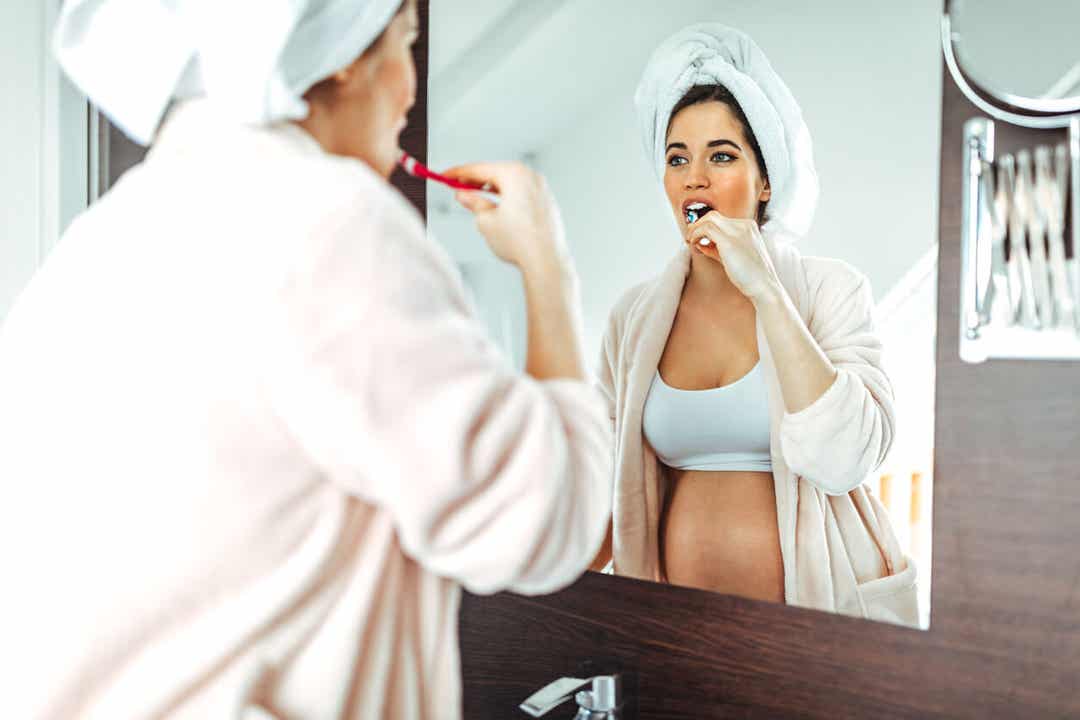Een zwangere vrouw die in de spiegel kijkt terwijl ze haar tanden poetst.