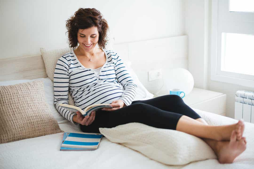 Kobieta w ciąży siedzi w łóżku i czyta księgę imion.