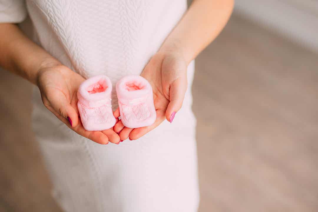A pregnant woman holding pink booties.