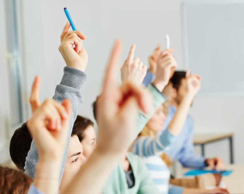 Studenter som løfter hendene i et klasserom.