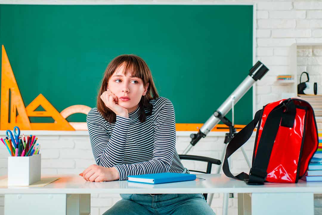 En tenåring sitter ved et skrivebord på skolen og ser lei ut.