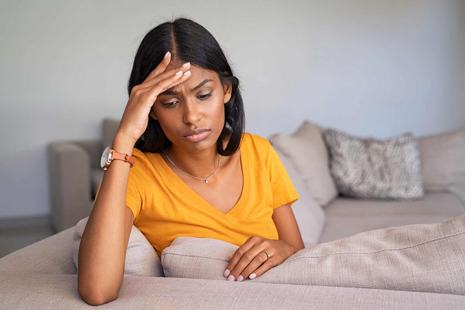En kvinde, der sidder på en sofa med sin hånd på panden, oplever hovedpine efter fødsel