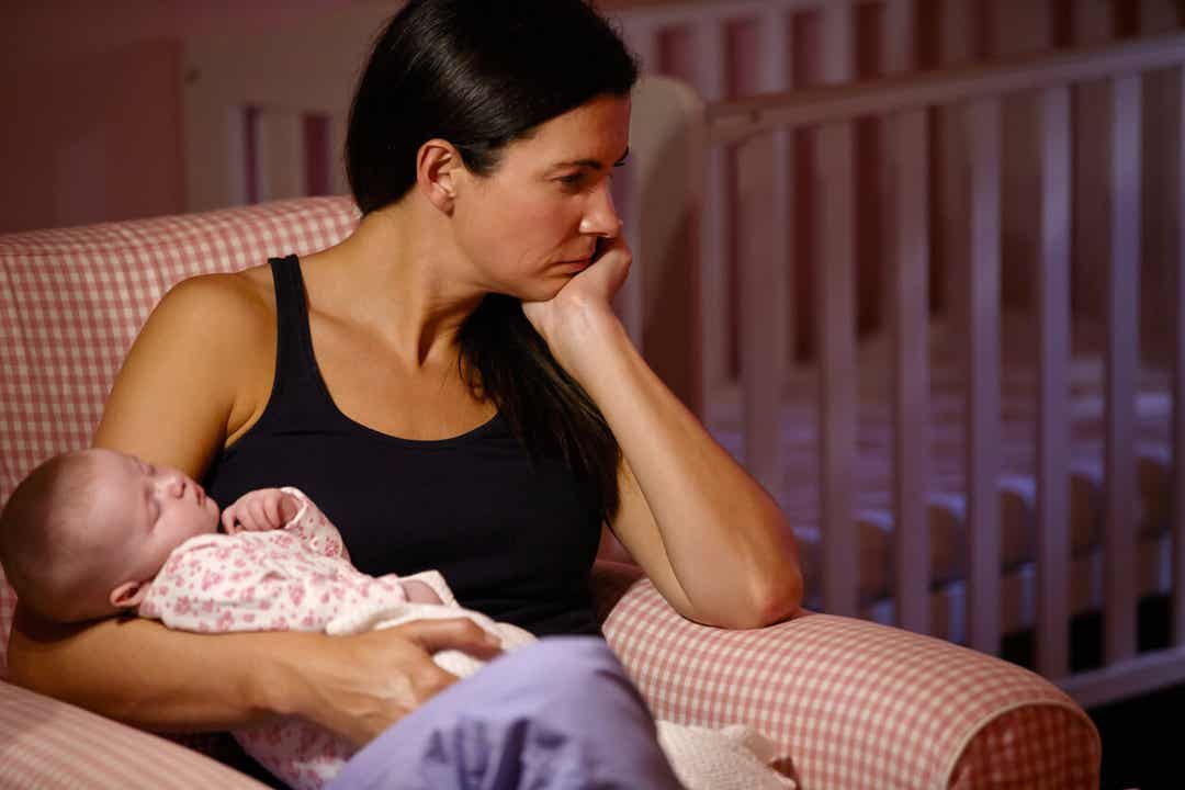 Een vrouw met postpartumdepressie die haar baby vasthoudt en droevig in de verte kijkt.
