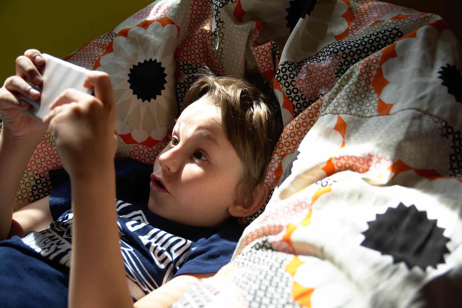 Dziecko bawiące się w łóżku z telefonem komórkowym.