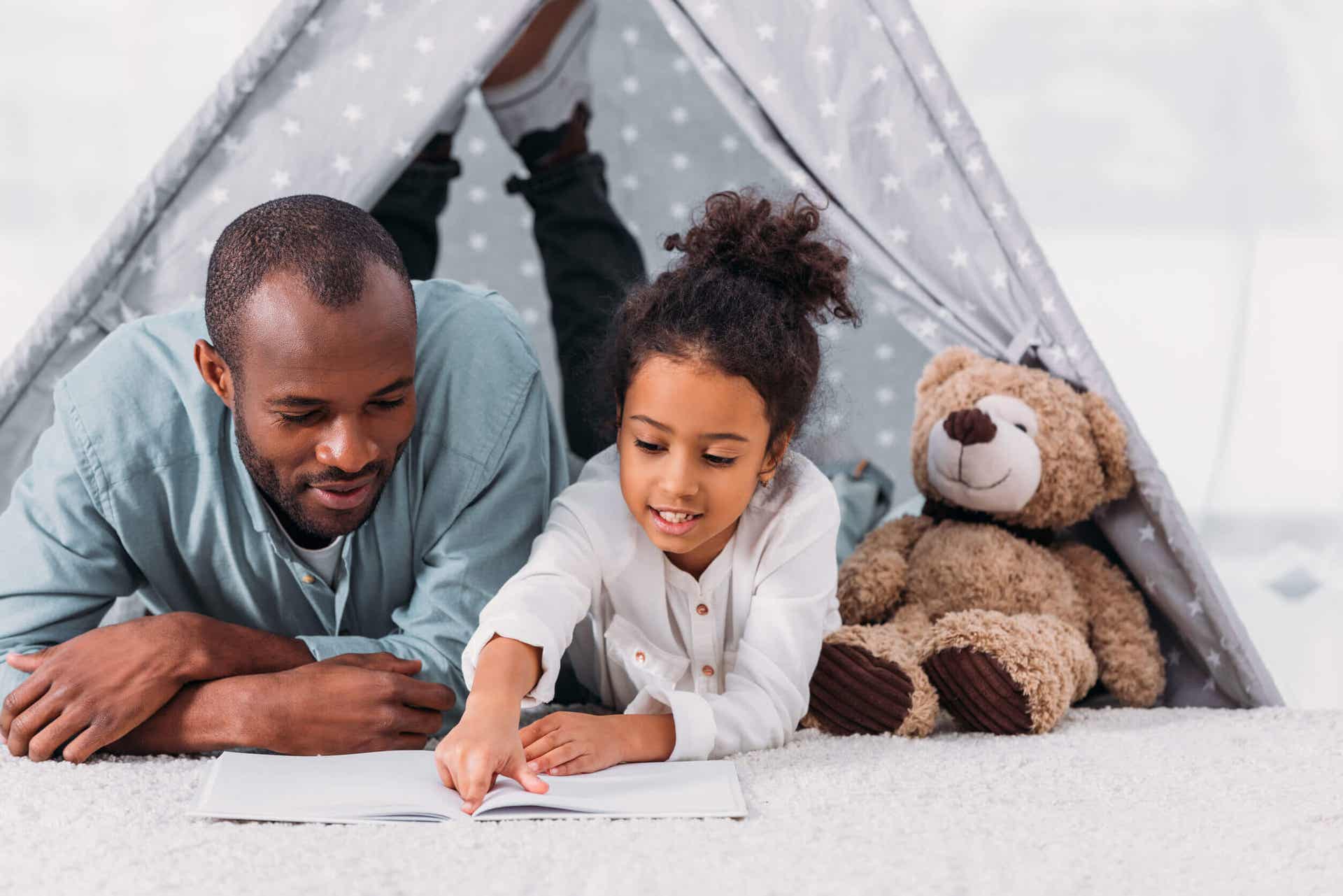 A father and daughter lying on the floor reading a book.