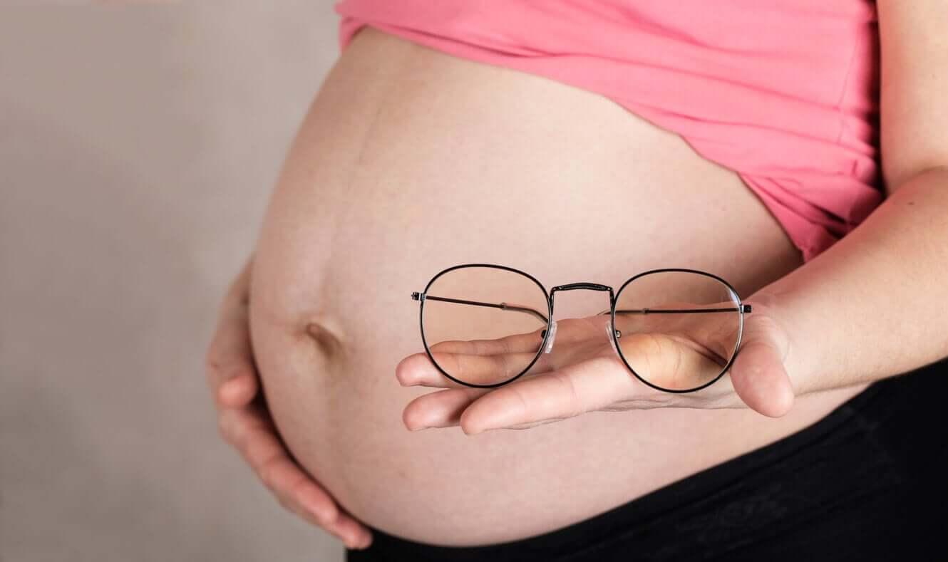 A pregnant woman holding eye glasses.