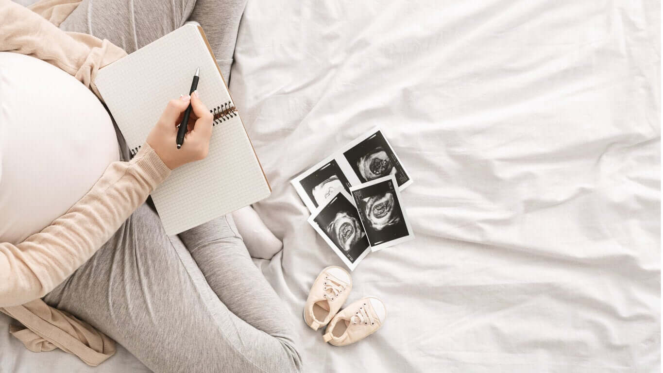 A pregnant woman looking at ultrasound images and writing in a notebook.