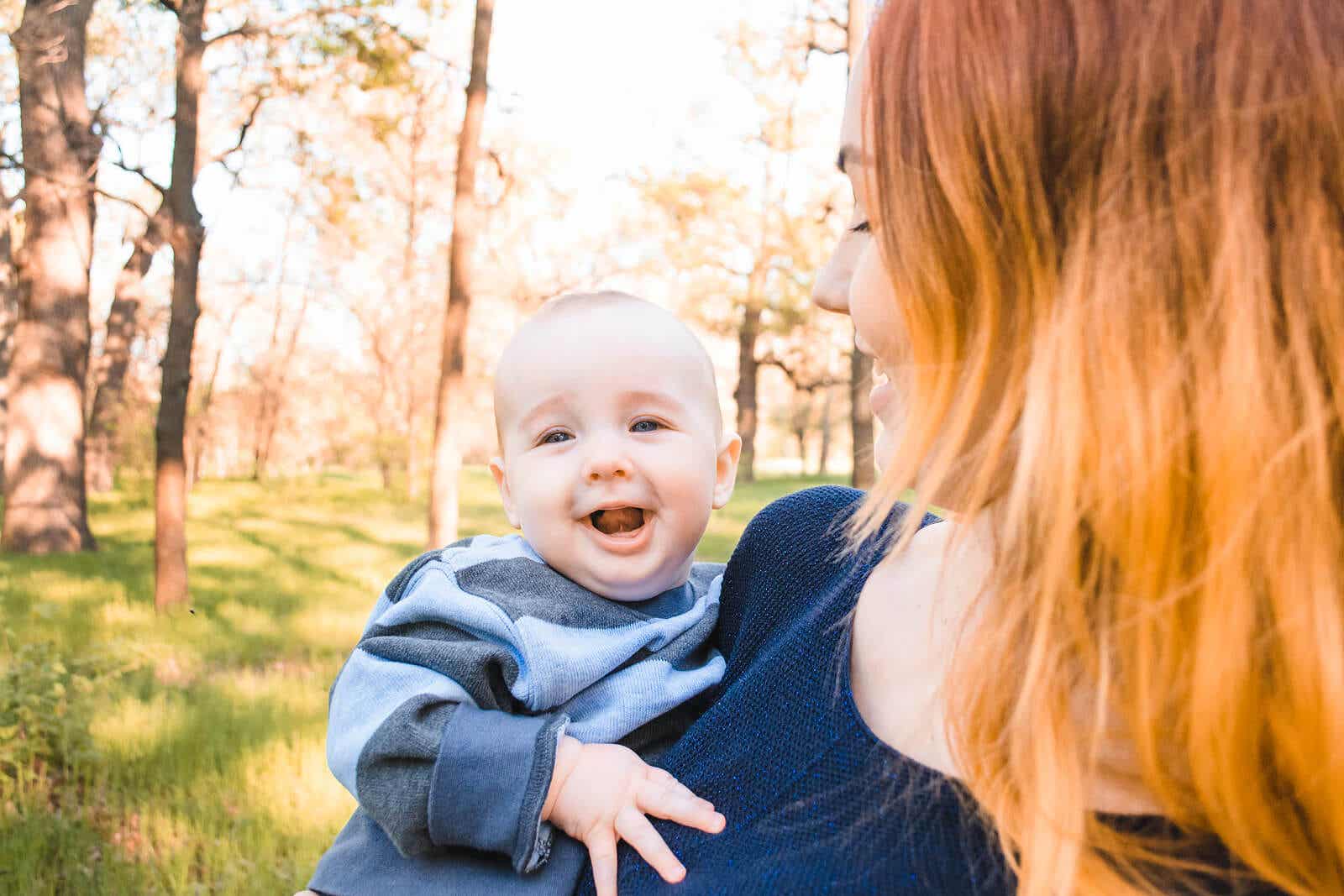 A mother walking in the woods, holding her smiling baby.